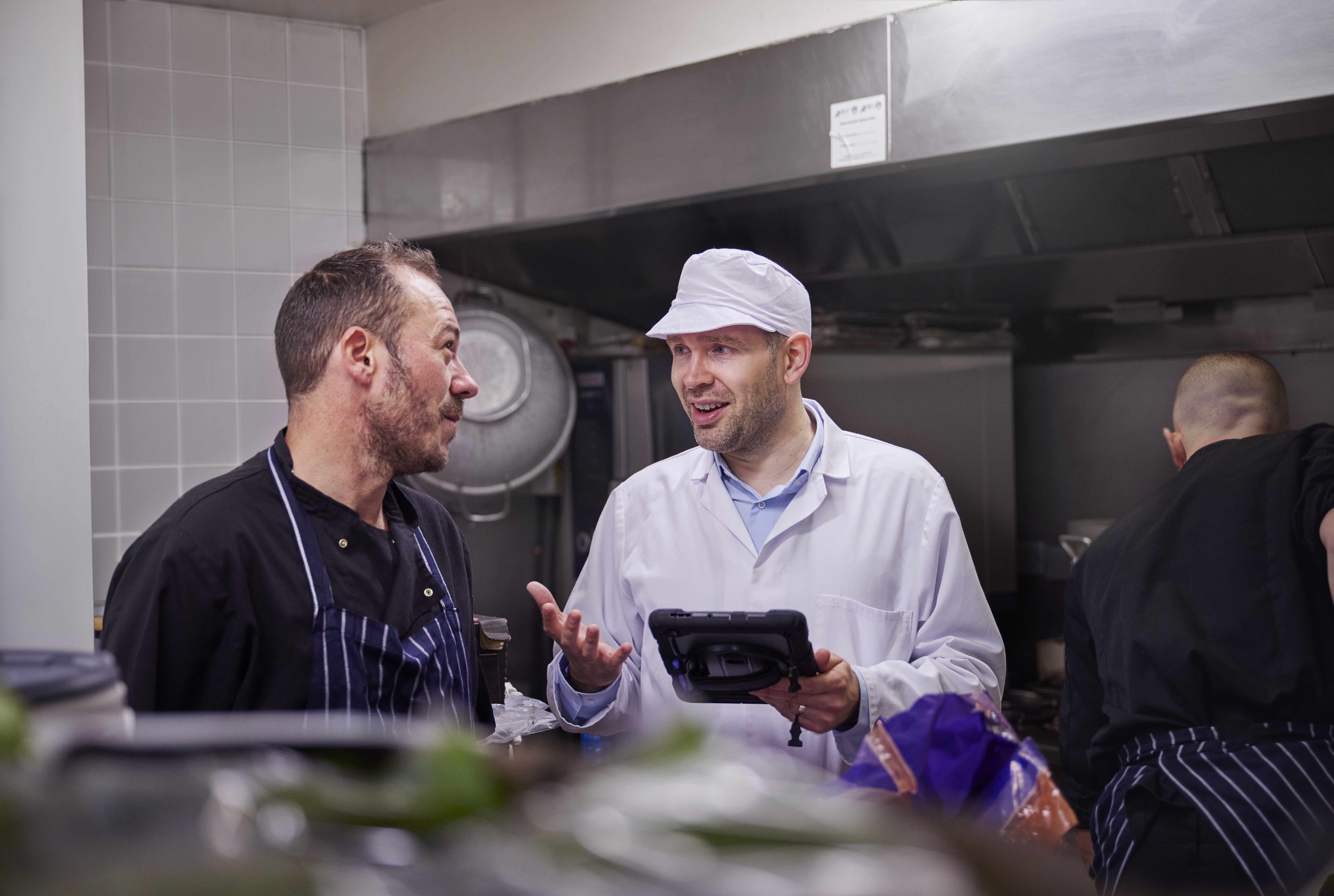 Daniel working in environmental health speaking to a chef in a restaurant kitchen