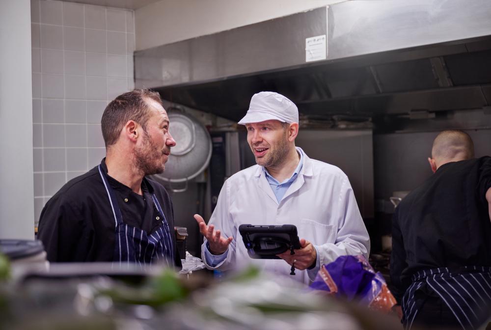 Daniel working in environmental health speaking to a chef in a restaurant kitchen